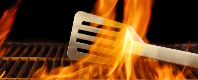 Stainless steel BBQ Grill spatula behind an orange flame in a BBQ Grill.