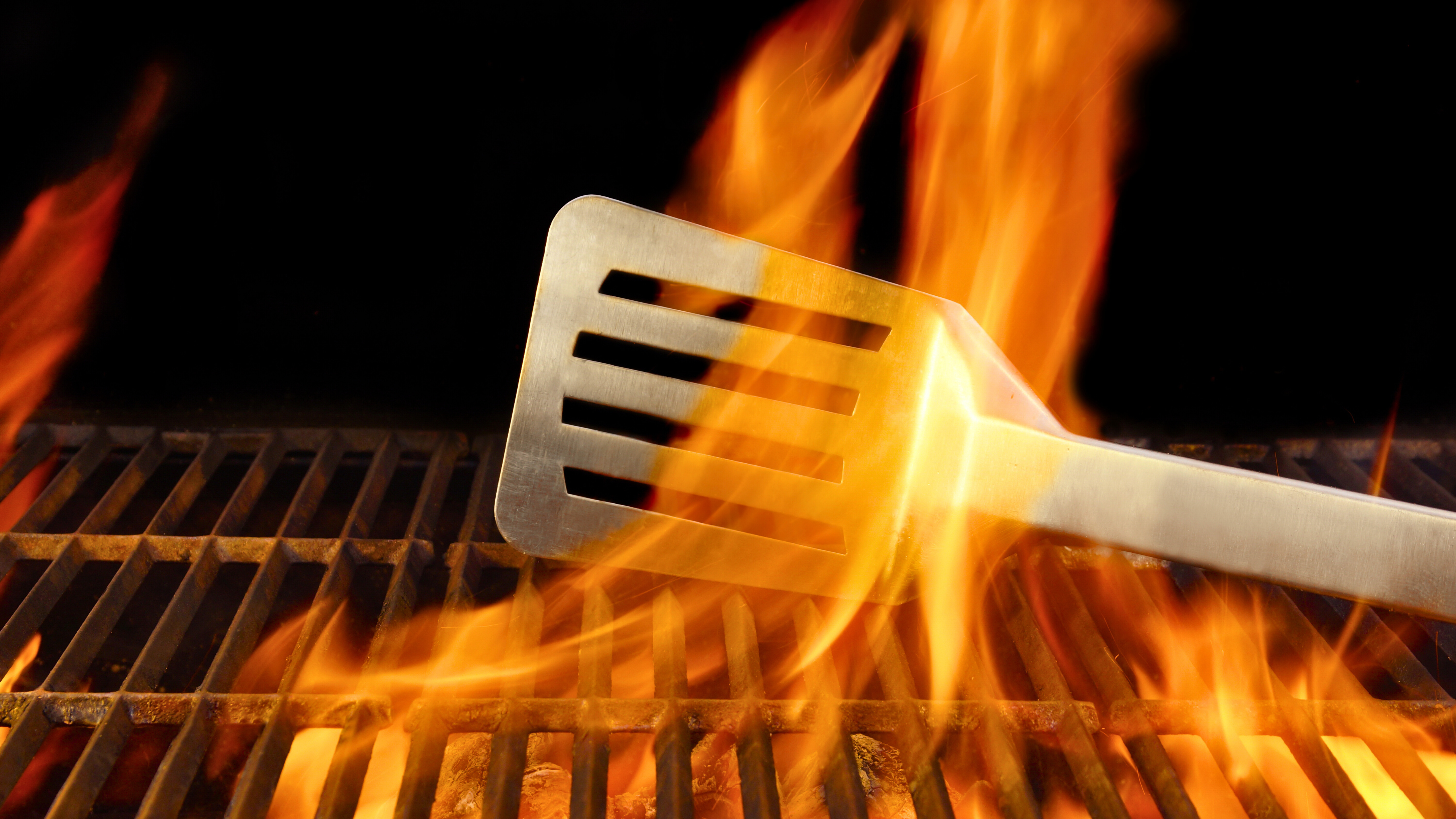 Stainless steel BBQ Grill spatula behind an orange flame in a BBQ Grill.