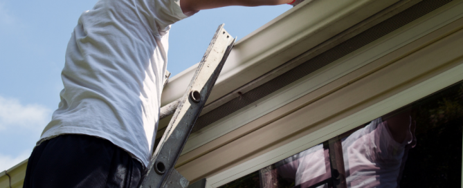 A man on a ladder cleaning out gutters