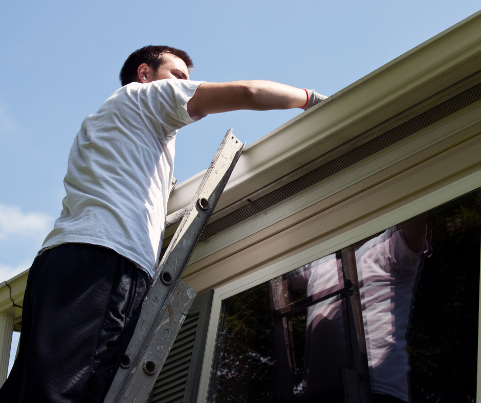 A man on a ladder cleaning out gutters