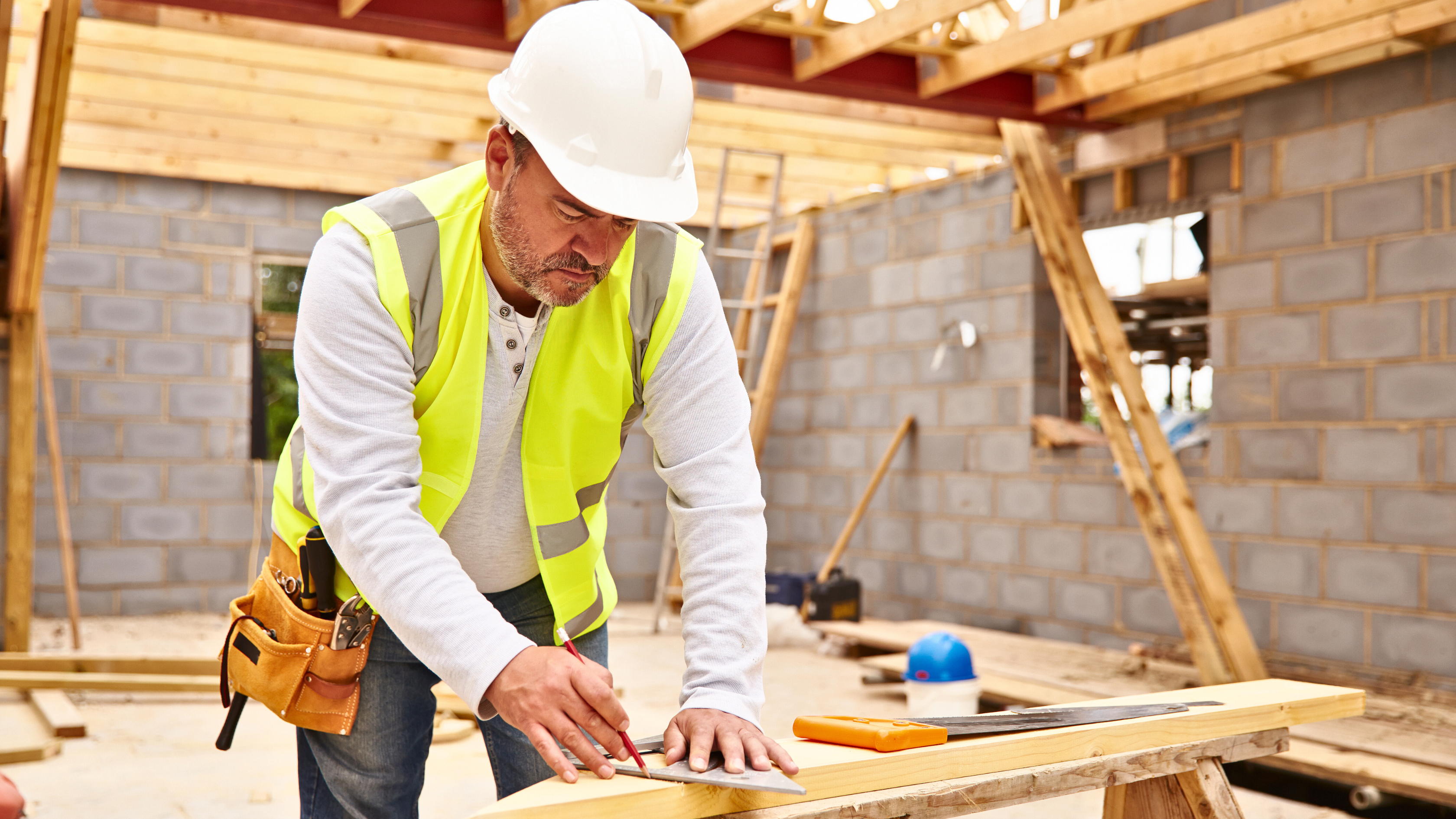 A construction worker measuring how much wood to cut at a construction site.