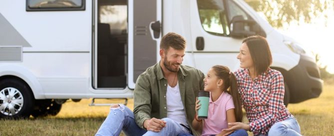 Two adults and a child on a picnic blanket in front of a camper