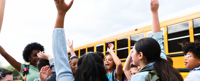 A group of diverse elementary school children celebrating the school year's end in the parking lot.