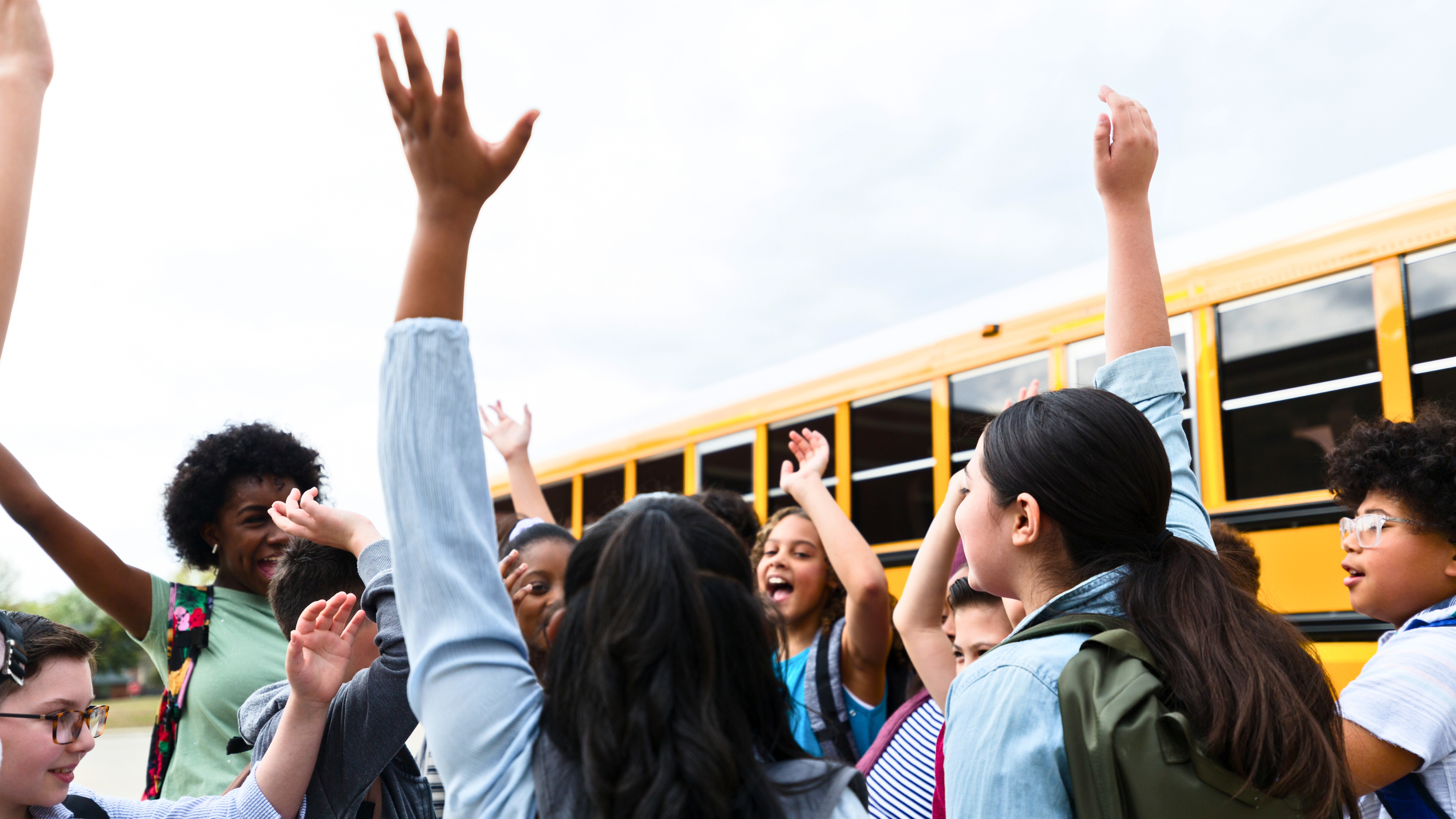 A group of diverse elementary school children celebrating the school year's end in the parking lot.