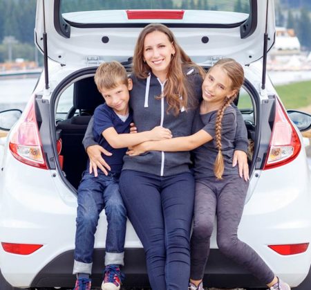 A mom and her two kids sitting in the trunk of their car.
