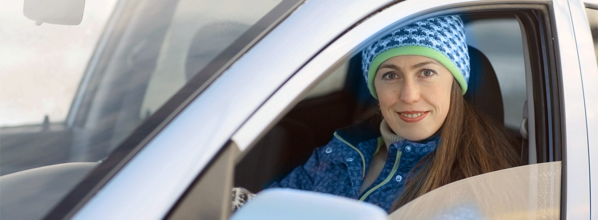 A woman sitting in her car looking out the window smiling.