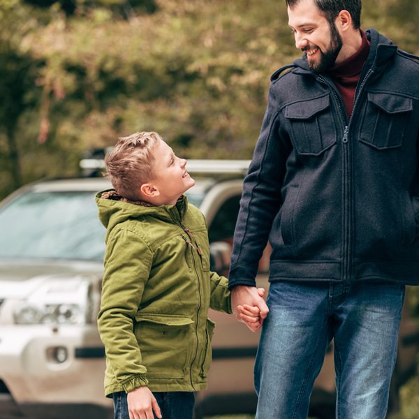 A father and son holding hands, smiling at one another.