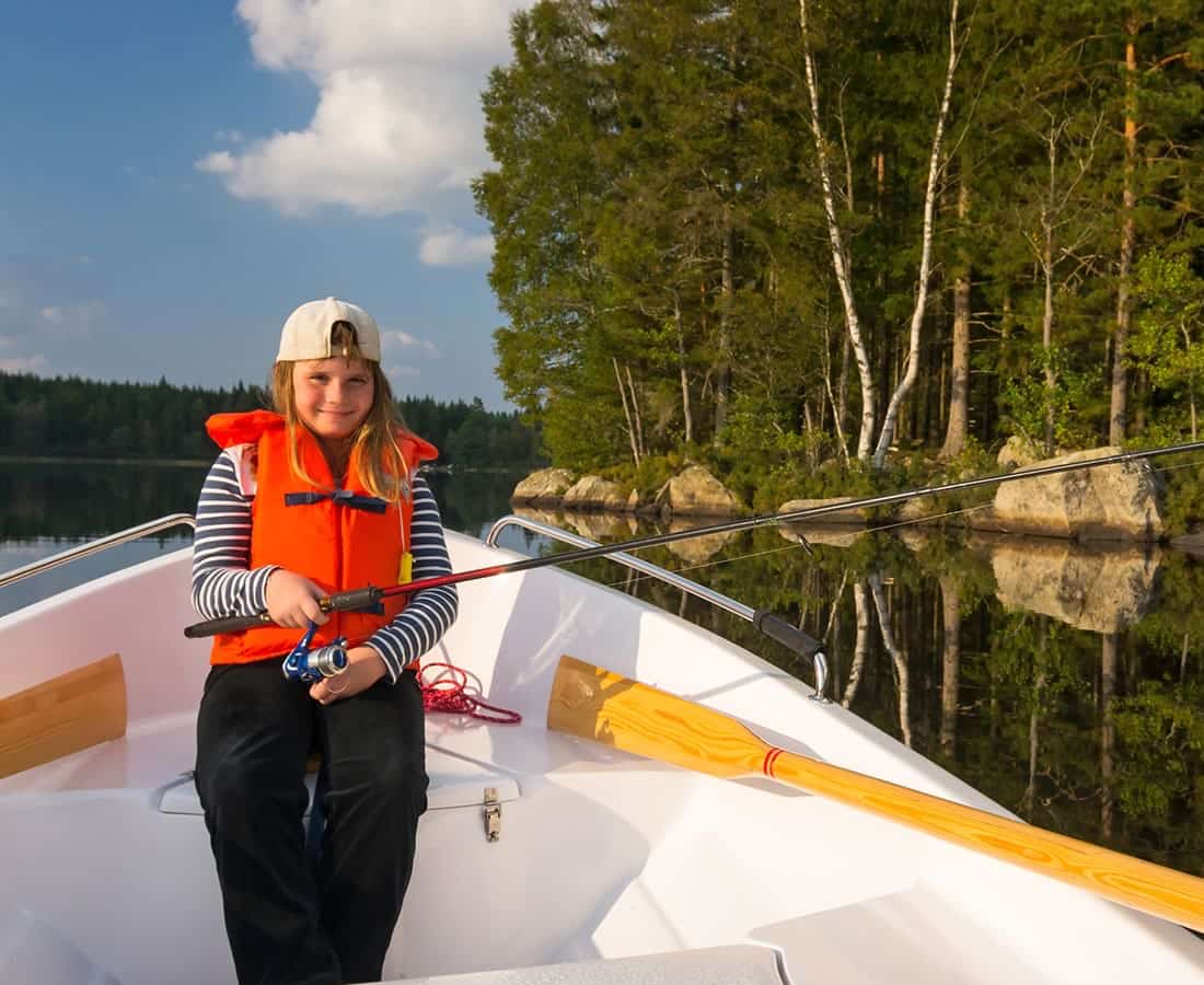 A girl on a boat wearing a life jacket and holding a fishing rod.