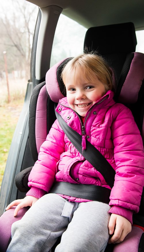 A young girl sitting in a car seat in a pink jacket.