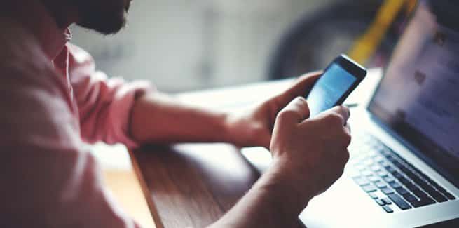 A person holding a smart phone at their desk..