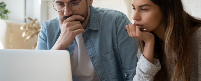 A man and woman look pensively at a laptop.