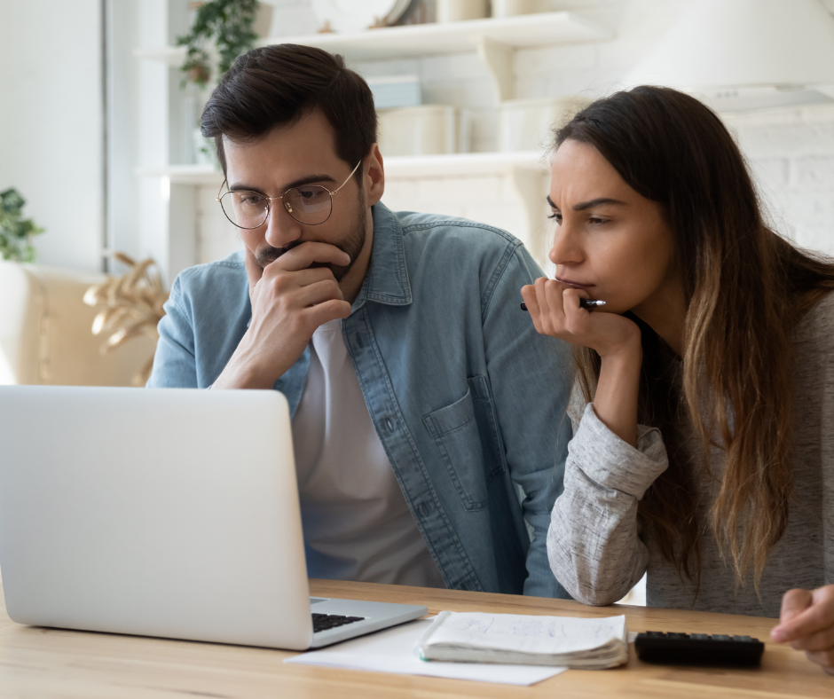 A man and woman look pensively at a laptop.