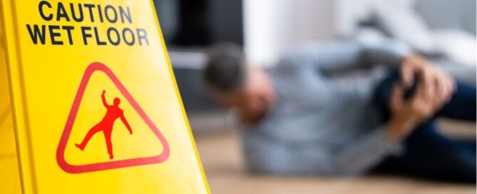 A person on the floor holding his knee next to a floor sign indicating the floor is wet
