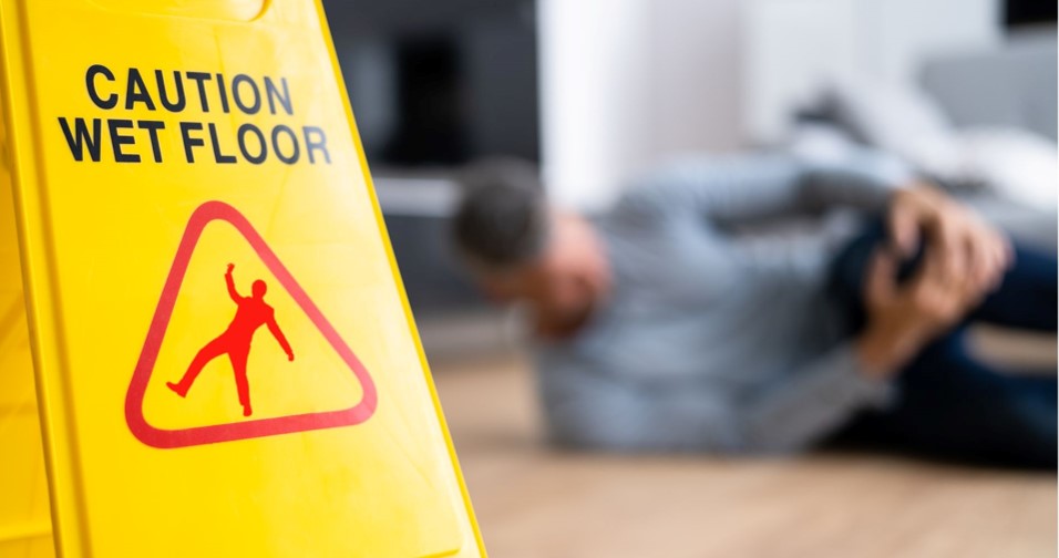 A person on the floor holding his knee next to a floor sign indicating the floor is wet