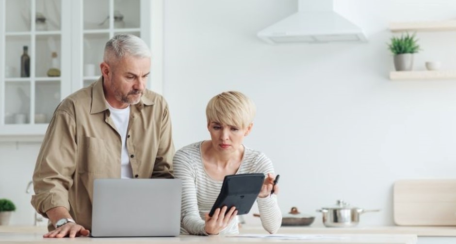 A man and a woman looking worried while looking at a calculator and their laptop