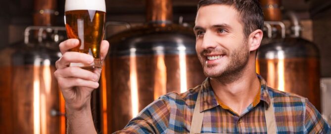 A man looking at a filled glass of beer in a brewery