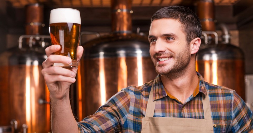 A man looking at a filled glass of beer in a brewery