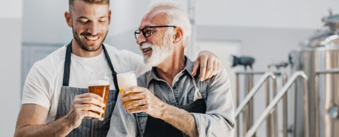 A young man cheersing beers with an older man in a brewery