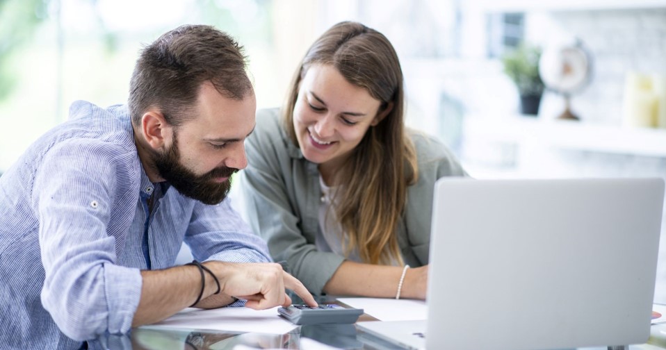 a man and woman sitting infront of a laptop smiling while looking down at the calculator